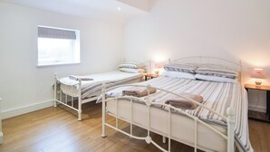 Un dormitorio con dos camas individuales, una ventana y una mesita de noche con lámpara.