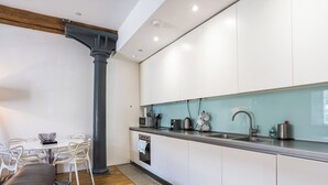 Une cuisine moderne avec des meubles blancs, un évier en acier inoxydable et un coin repas comprenant une table et des chaises blanches.