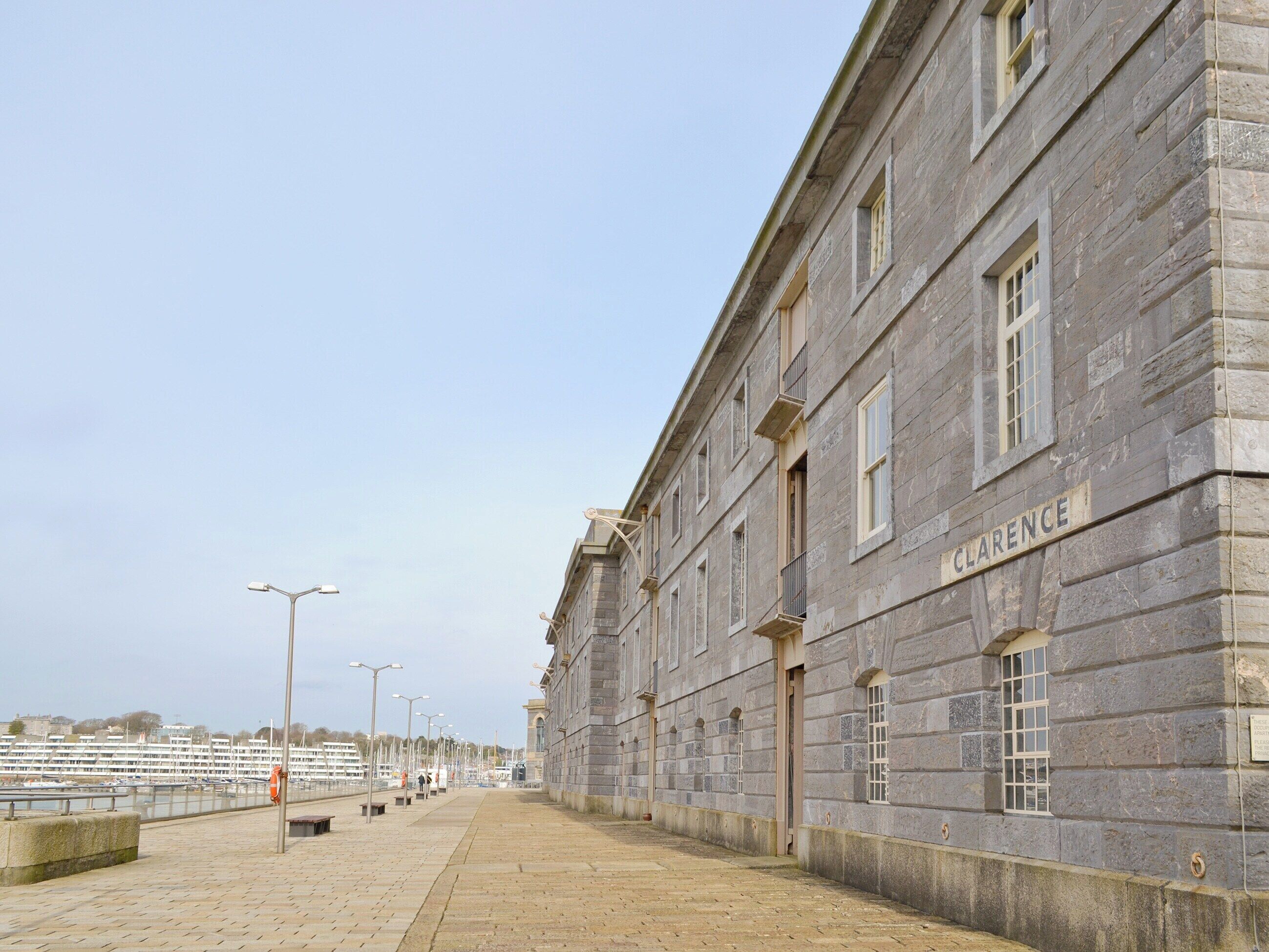 Un bâtiment en pierre dont la façade porte l’inscription « CLARENCE », situé à côté d’une promenade en bord de mer, agrémentée d’une allée pavée.
