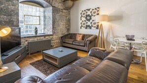 Un salon moderne avec un mur en pierre, une cheminée, un canapé, une table basse, un téléviseur et une table à manger avec des chaises.