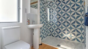 Ein modernes Badezimmer mit Toilette, Waschbecken und Dusche mit geometrischen Fliesenmustern.