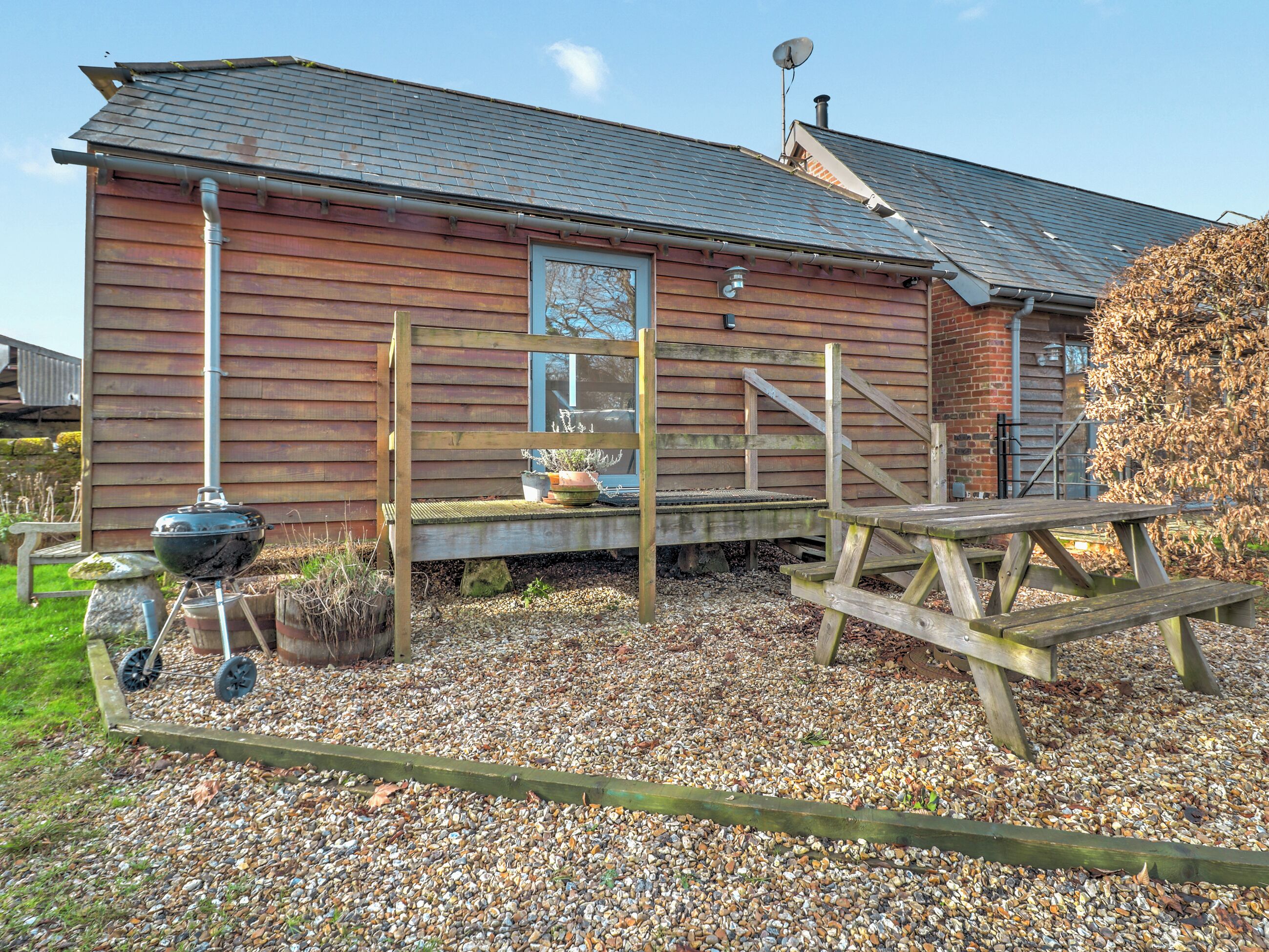 A wooden house with a gravel driveway, a barbecue grill, and a wooden deck.