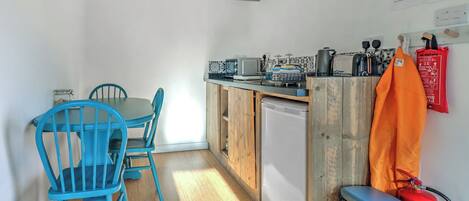 A compact kitchen with wooden cabinets, a small refrigerator, and a blue table with chairs.