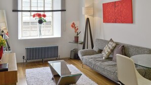 Una sala de estar moderna con una mesa de centro de cristal, un sofá gris, un sillón blanco y un cuadro abstracto rojo en la pared.