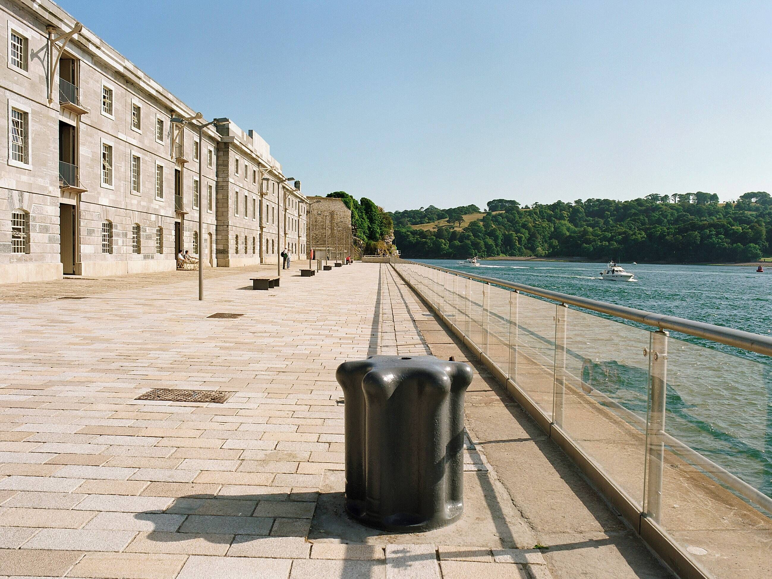 Une promenade en bord de mer avec un chemin pavé de pierres, une rambarde en métal et une grande poubelle.