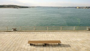 Un banco en un paseo marítimo adoquinado con vista al mar y tierra a lo lejos.