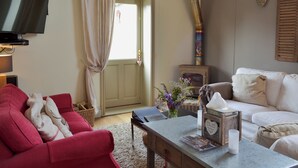 Un salón con un sofá rojo, un sofá blanco, una televisión, una chimenea y una puerta con cortinas.
