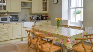 A kitchen with a dining table, chairs, a clock, and a window. - Mayflower Apartment-UKC93 (Plymouth)