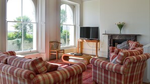 A living room with large windows, a fireplace, and plaid furniture. - Mayflower Apartment-UKC93 (Plymouth)