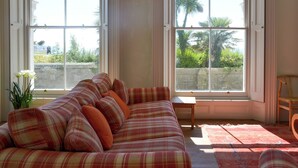 A room with a plaid sofa, two large arched windows, a small table, and a chair. - Mayflower Apartment-UKC93 (Plymouth)