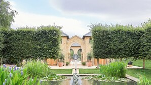 Un jardín con un estanque, plantas en macetas y un edificio con fachada de piedra.