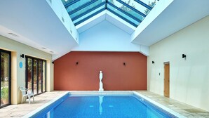 Una piscina interior con vistas despejadas al cielo a través del techo, una estatua en el centro y una puerta a la derecha.