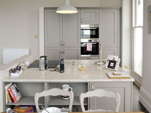 A kitchen with a central island, two white chairs, a coffee maker, a kettle, a toaster, and a framed photo on the island. - Sir Francis Drake-UKC96 (Plymouth)