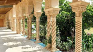 Un espace extérieur abrité, doté de colonnes et d’arcs en pierre, et entouré de verdure.
