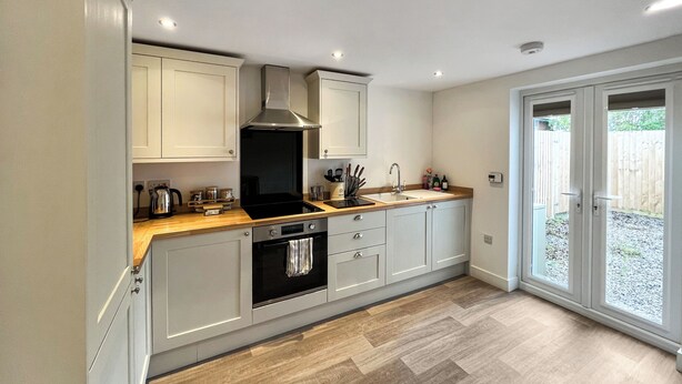 A modern kitchen with light grey cabinets, a stainless steel range hood, a built-in oven, and a wooden countertop. - 3 bedroom accommodation in North Scarle (North Scarle)