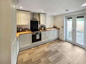 Une cuisine moderne avec des meubles de couleur gris clair, une hotte en acier inoxydable, un four encastré et un plan de travail en bois.