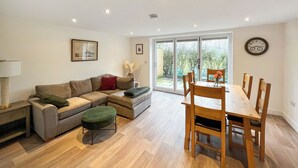 A modern living room with a sofa, ottoman, dining table, chairs, and a view through a glass door to the outside. - 3 bedroom accommodation in North Scarle (North Scarle)