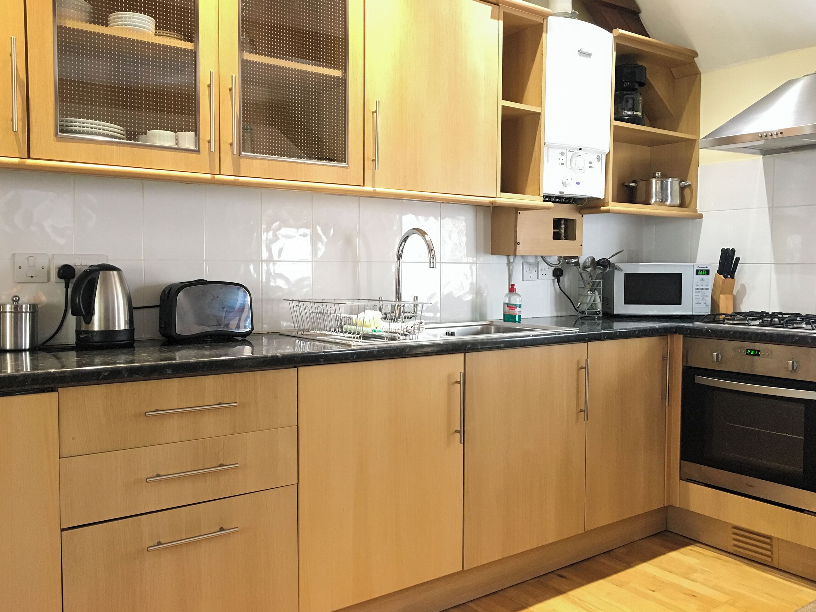 A modern kitchen with wooden cabinets, a stainless steel kettle, a toaster, a microwave, and a gas stove.