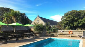 En swimmingpool med ett trädäck, picknickbord och gröna parasoller.