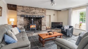 A living room with a stone fireplace, leather sofas, a wooden coffee table, and a television. - 3 bedroom accommodation in Kidwelly (Kidwelly)