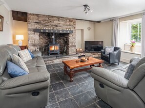 A living room with a stone fireplace, leather sofas, a wooden coffee table, and a television. - 3 bedroom accommodation in Kidwelly (Kidwelly)