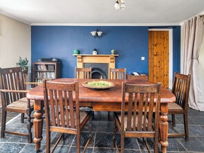 A dining room with a wooden table and chairs, a fireplace, a bookshelf, and a door. - 3 bedroom accommodation in Kidwelly (Kidwelly)