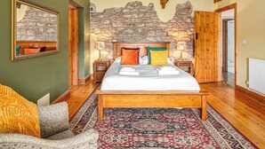 A bedroom with a stone wall, wooden bed frame, and a patterned rug. - 3 bedroom accommodation in Kidwelly (Kidwelly)