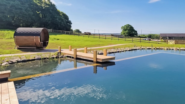 Una piscina trasparente con pontile in legno e una botte.