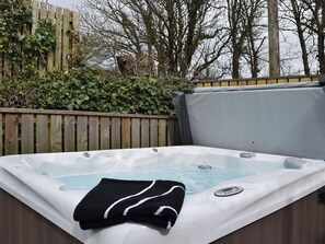 A hot tub with a control panel, surrounded by a wooden fence and greenery. - 2 bedroom accommodation in Kidwelly (Kidwelly)