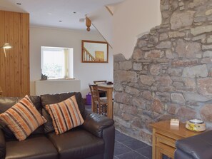 A living room with a leather sofa, wooden panel walls, a stone wall, a dining area with a table and chairs, and a window with blinds. - 2 bedroom accommodation in Kidwelly (Kidwelly)