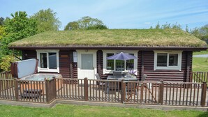 A log cabin with a thatched roof, a patio with outdoor furniture, and a fenced deck area. - Pheasant Lodge-W43009 (Brayton, Selby)