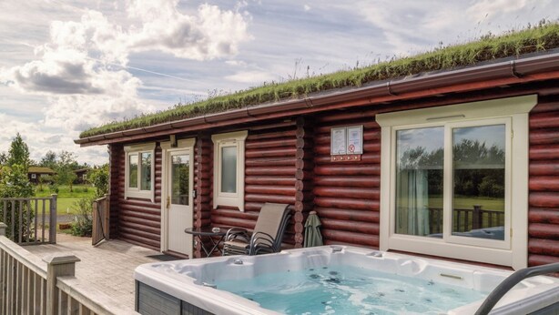 Una cabaña de troncos con jacuzzi y mobiliario de exterior.