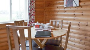 Comedor de una cabaña de madera con una mesa dispuesta para el té, sillas y una ventana con cortinas.