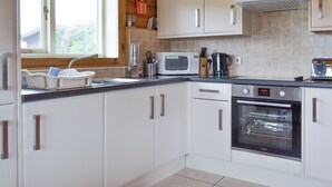 Una cocina moderna con armarios blancos, horno de acero inoxidable, microondas y pileta.