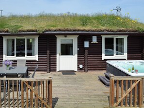 Una cabaña de troncos con jacuzzi, terraza de madera y techo cubierto de césped.