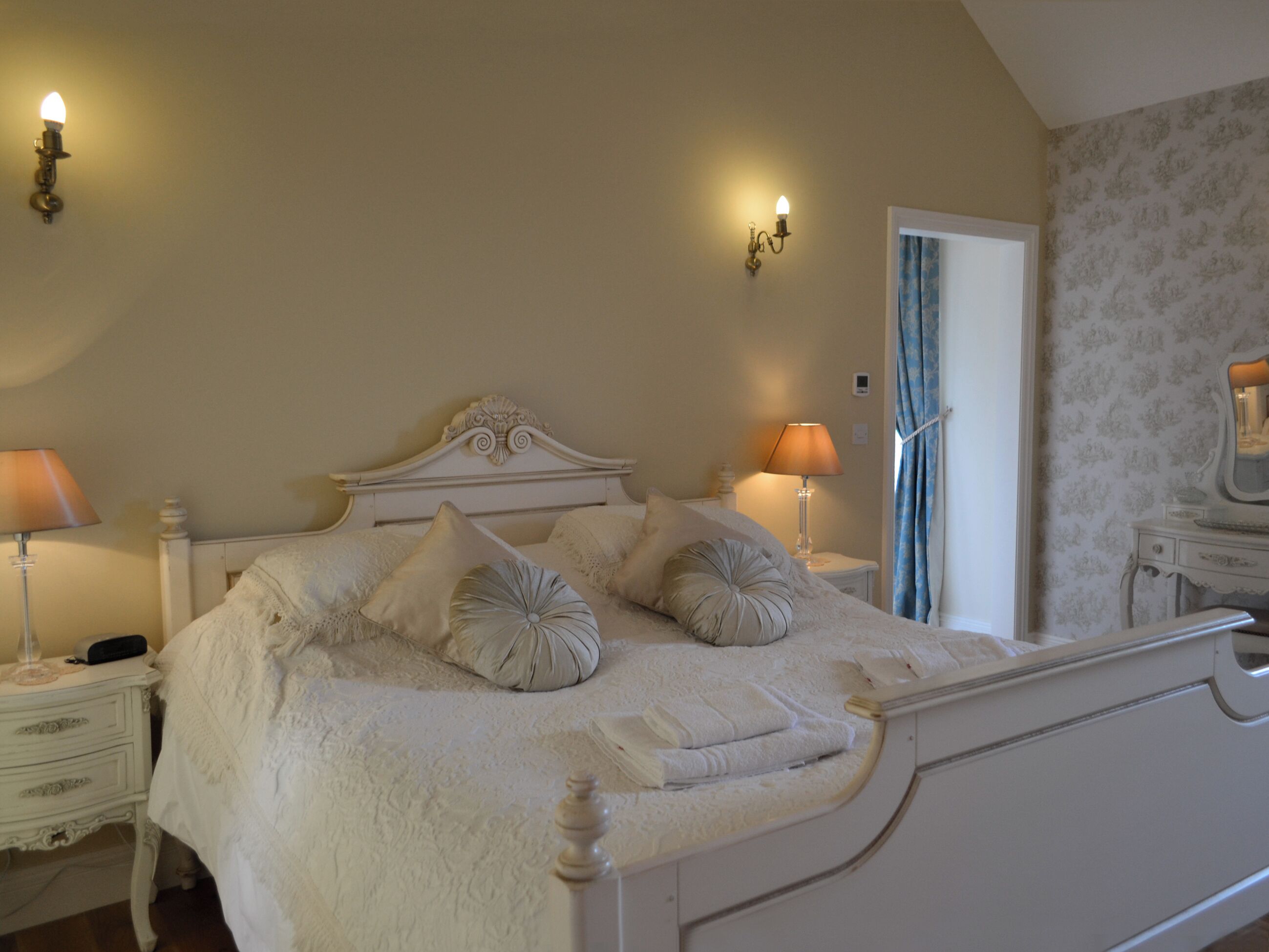 A bedroom with a bed, two bedside tables, a nightstand, a mirror, and a door with curtains.