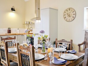 A dining area with a wooden table set for four, surrounded by wooden chairs. A wall clock is visible on the wall. - 2 bedroom accommodation in Kidwelly (Kidwelly)