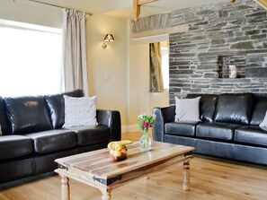 A living room with two black leather sofas, a wooden coffee table with fruit, and a stone wall. - 2 bedroom accommodation in Kidwelly (Kidwelly)