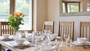 Une table à manger dressée avec de la vaisselle blanche, des verres et un vase rempli de fleurs.