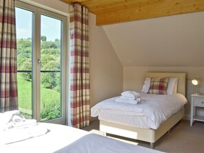 A bedroom with a bed, a nightstand, and a window with curtains.