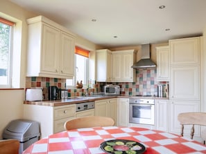 Una cocina con armarios blancos, salpicadero de azulejos, microondas, estufa y una mesa con mantel a cuadros.