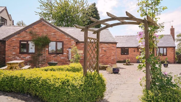 A brick cottage with a wooden pergola, a gravel path, and a yellow table. - 2 bedroom accommodation in Bickley, near Malpas (Bickley, near Malpas)