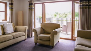 A living room with a sofa, armchair, and a large window with curtains.
