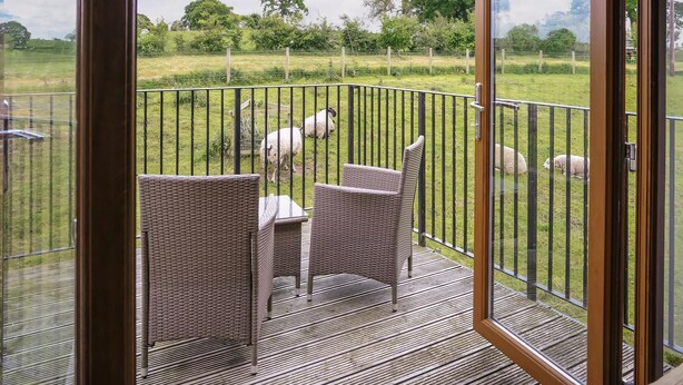 A balcony with wicker furniture and a view of sheep grazing in a field.