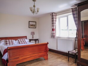 Une chambre à coucher avec un lit en bois, une table de chevet avec une lampe, une fenêtre avec des rideaux et un radiateur.