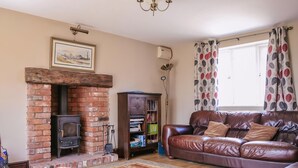 A living room with a brick fireplace, leather sofa, patterned rug, and a bookshelf.