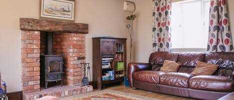 A living room with a brick fireplace, leather sofa, patterned rug, and a bookshelf.