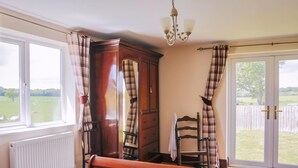 A bedroom with a bed, a wooden wardrobe, a chair, a radiator, and a view of the outdoors.