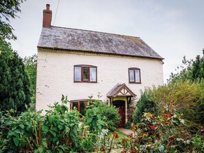 A white house with a sloped roof, two windows, a chimney, and a small porch.