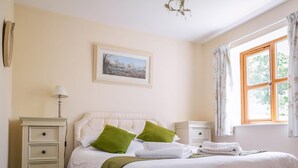 Een slaapkamer met een bed, een nachtkastje, een dressoir, een schilderij aan de muur en een raam met gordijnen.